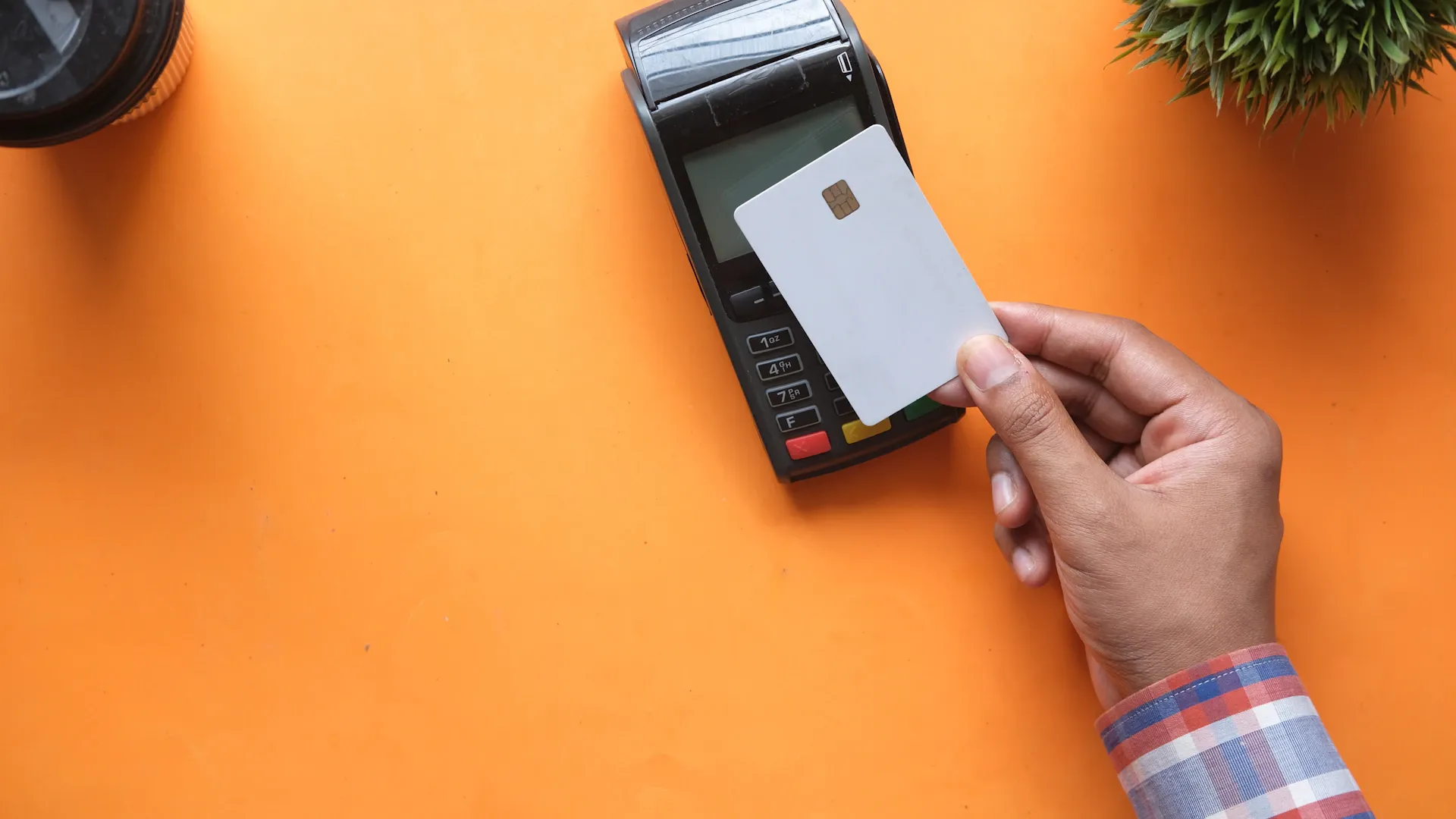 Une personne tenant une carte de crédit vierge près d’un terminal de paiement sur orange