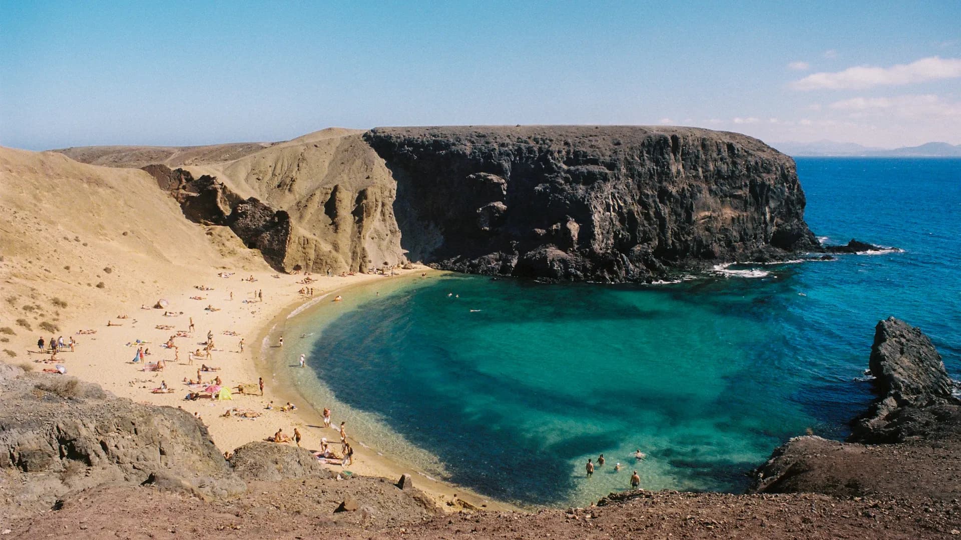 une plage de sable avec une eau bleue claire à côté d’une falaise