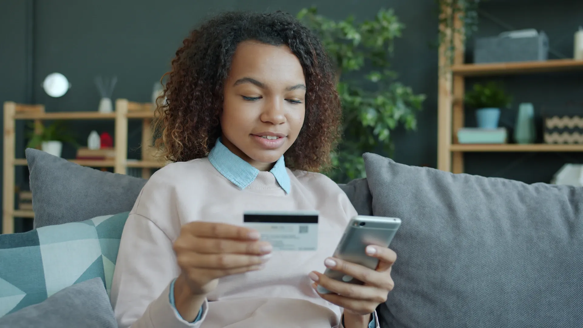 Jeune femme tenant carte de crédit et smartphone à l’intérieur