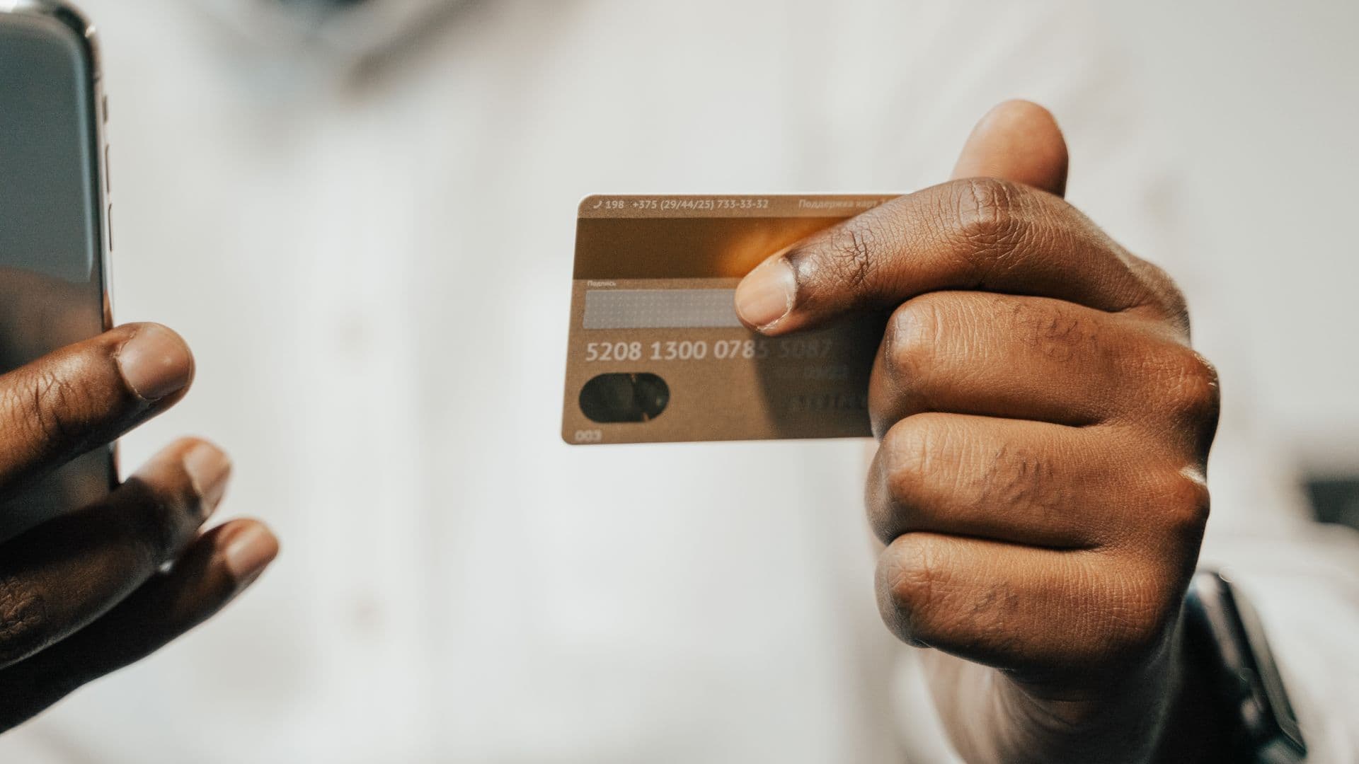 Une personne utilise son téléphone en tenant une carte bancaire