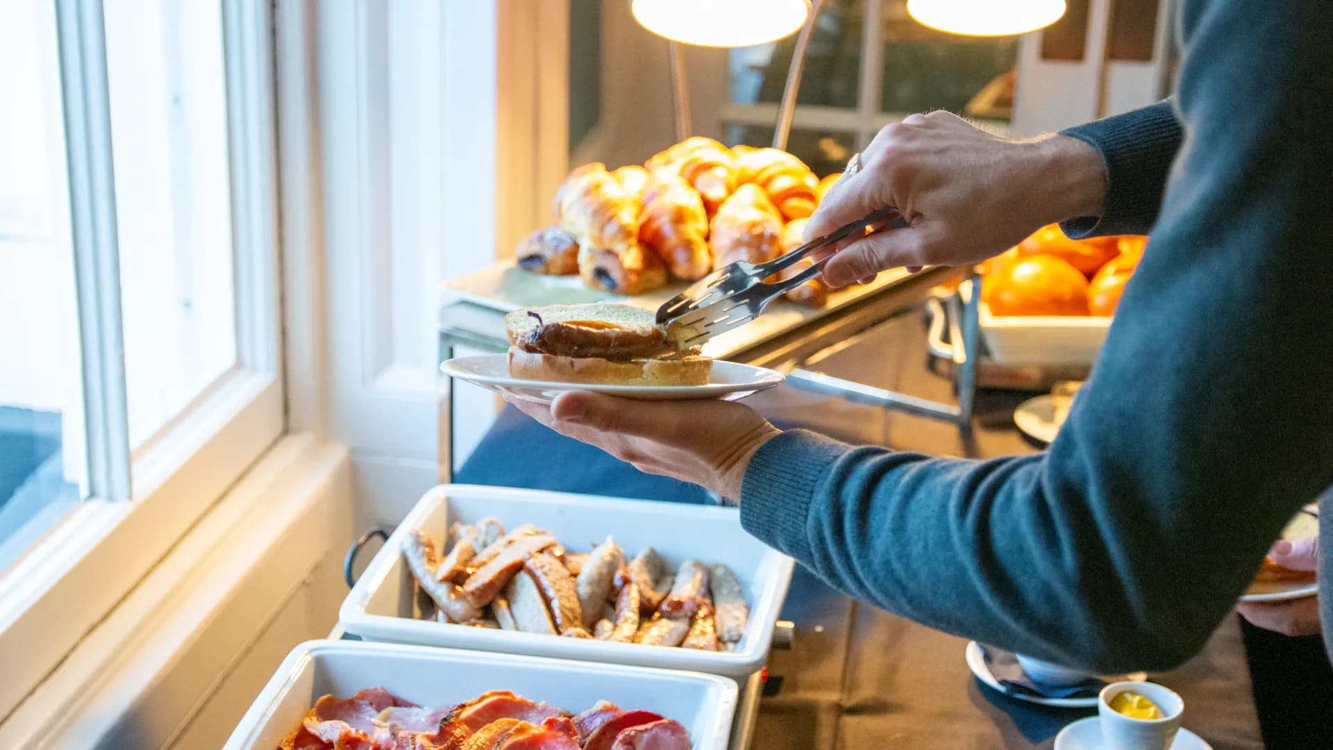 Personne servant le buffet du petit-déjeuner avec bacon et pâtisseries
