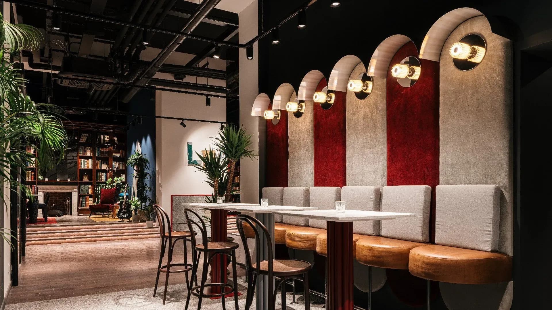 Le bar et le lobby du Ruby Lilou à Marseille : une rangée d'alcôves voûtées en velours rouge et beige, éclairées par des appliques rondes, face à des tables hautes et des plantes