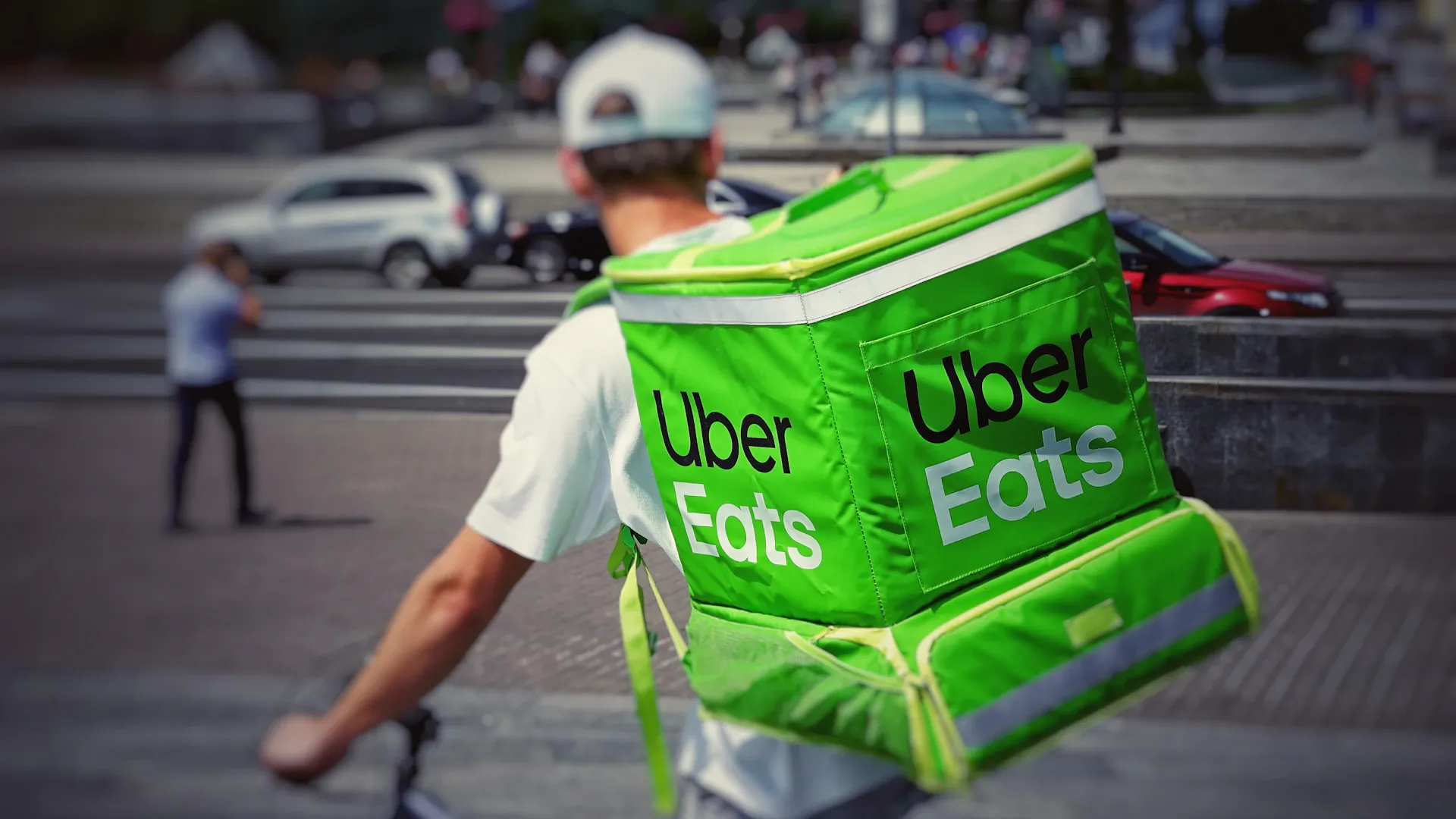 Livreur à vélo vu de dos avec un sac de livraison vert Uber Eats.
