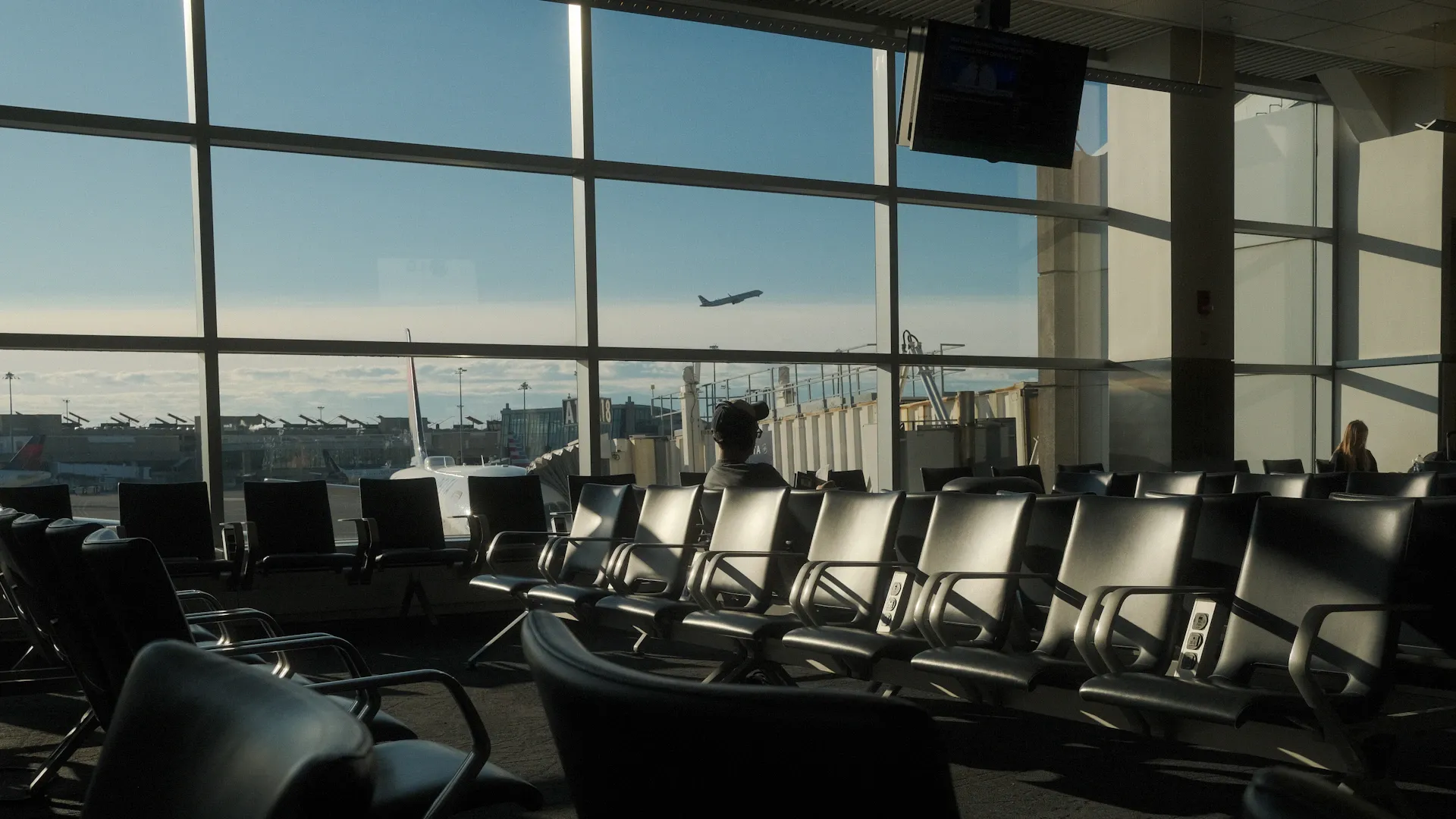 Voyageurs assis dans le terminal de Boston-Logan face à un avion au décollage