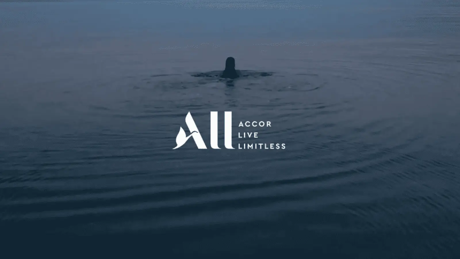 Une personne nage dans une eau calme au crépuscule avec le logo ALL Accor Live Limitless