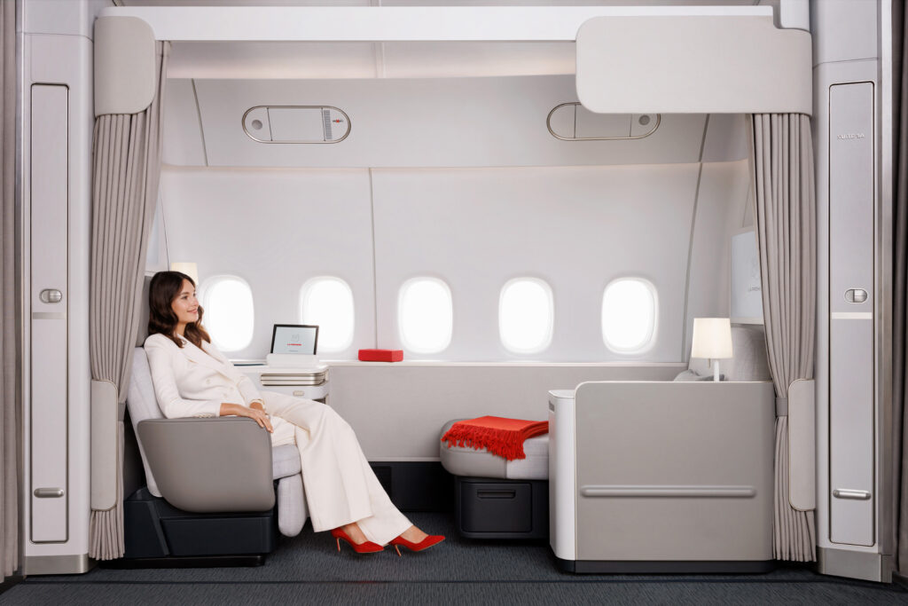 Une femme assise dans une suite La Première d'Air France, décor blanc et rouge élégant.