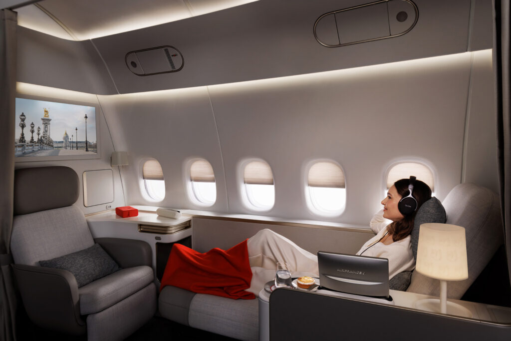 Femme détendue allongée dans la cabine La Première d'Air France, regardant un écran avec vue de Paris.