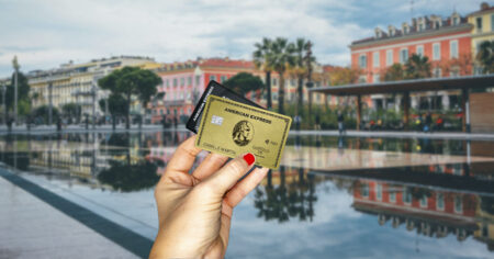 Une main tient deux cartes American Express devant un paysage urbain avec un bassin réfléchissant