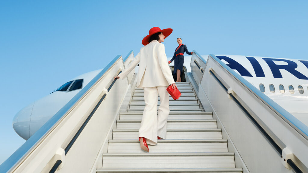 Une passagère élégante monte la passerelle vers un avion Air France, accueillie par une hôtesse.