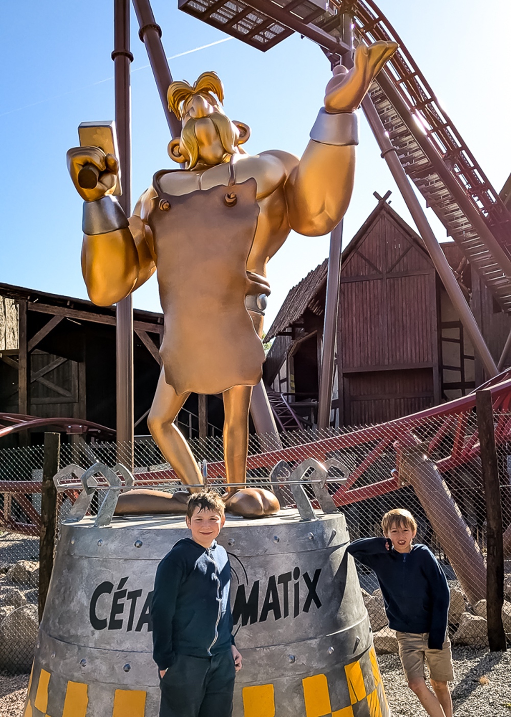 Deux enfants posent devant la grande statue dorée de Cétautomatix au Parc Astérix en France.