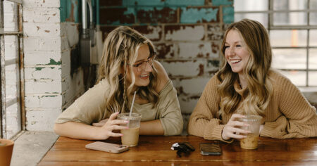 Deux amies souriantes discutent autour de boissons glacées dans un café