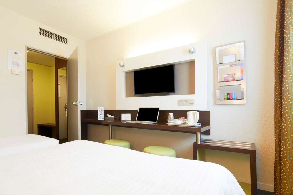 Chambre d'hôtel lumineuse avec lit double, bureau moderne, télévision murale et plateau de courtoisie.