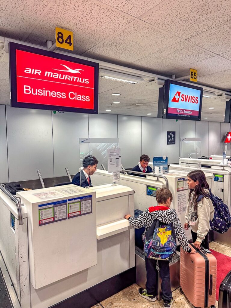 Deux enfants enregistrent leurs bagages au comptoir Business Class d'Air Mauritius à côté de Swiss.