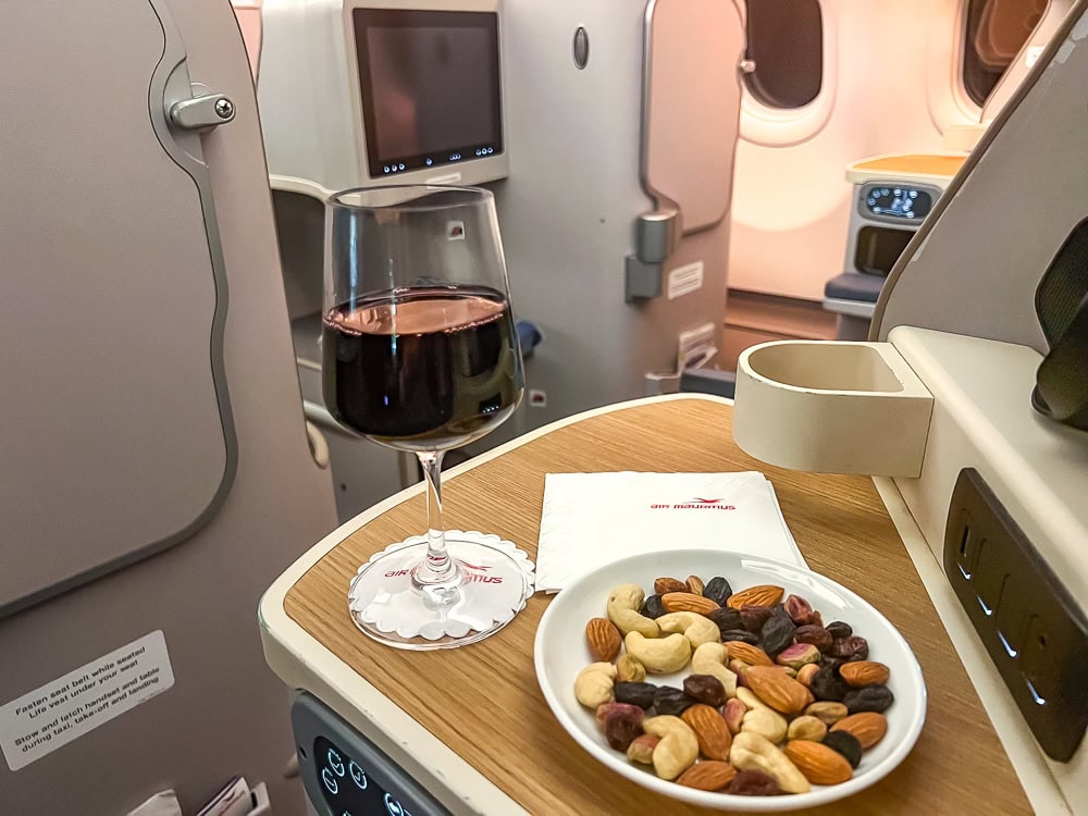 Siège de classe affaires Air Mauritius avec verre de vin rouge et plateau de noix à bord.