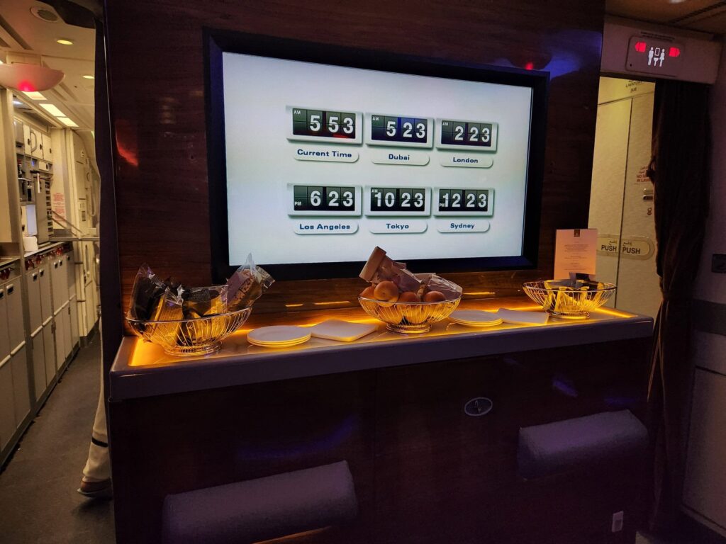 Bar et écran d'horloge mondiale dans la cabine Première Classe d'un avion Emirates en vol de nuit