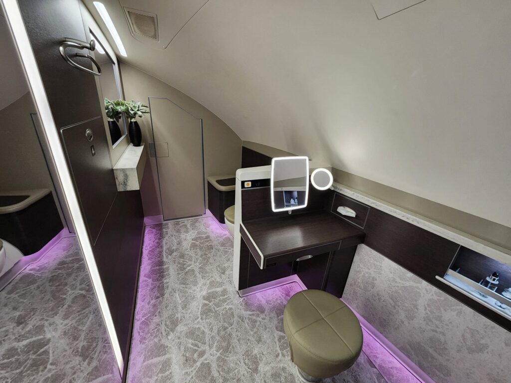 Espace privé de Première Classe Singapore Airlines avec coiffeuse, miroir illuminé et éclairage mauve