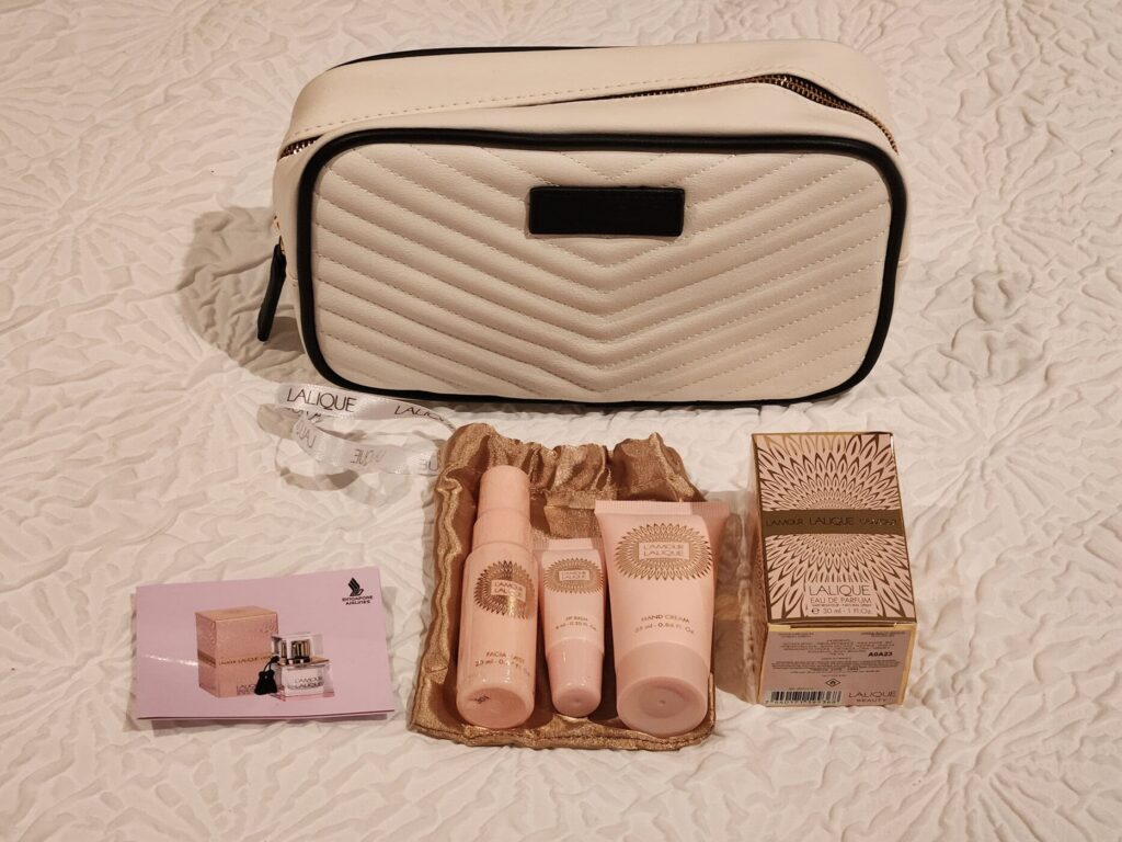 Trousse de voyage Singapore Airlines avec produits Lalique L'Amour sur lit blanc texturé