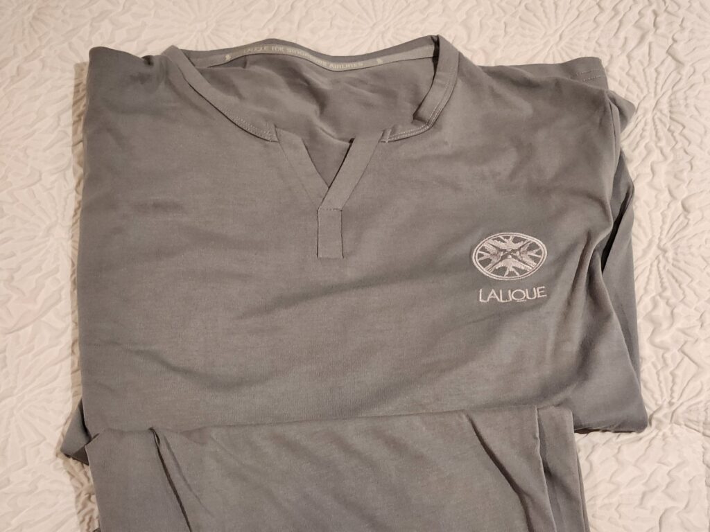 Pyjama gris Singapore Airlines signé Lalique plié sur un lit blanc en cabine premium