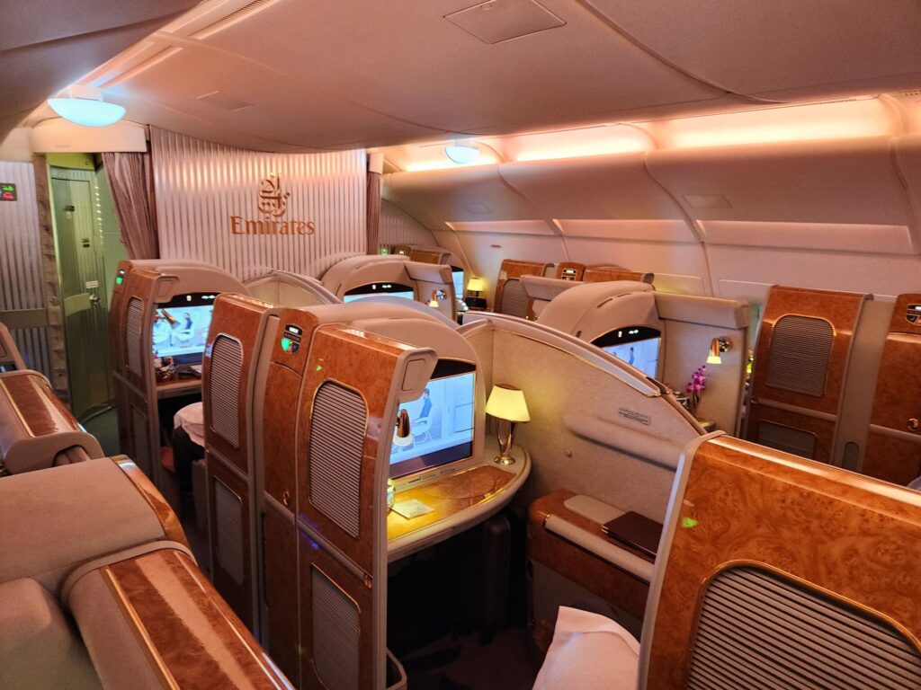 Cabine de première classe Emirates avec suites fermées et écrans individuels sur un avion long-courrier.
