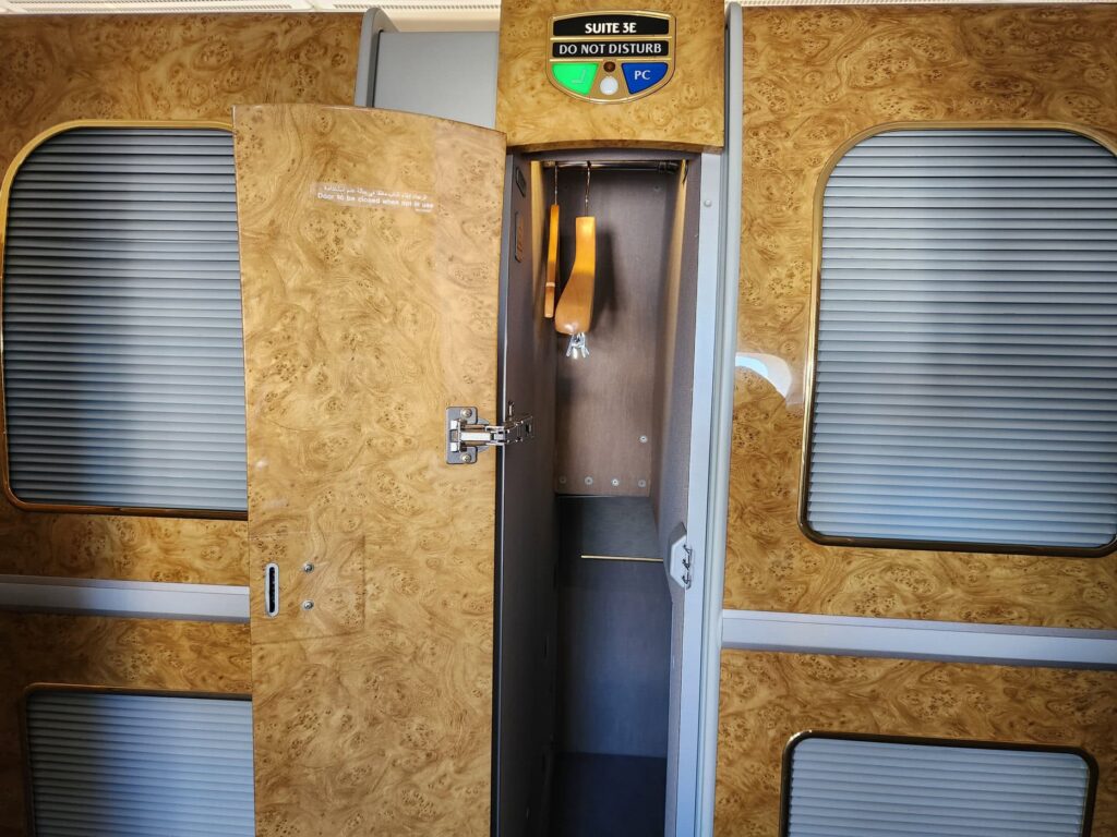 Porte de suite privée Emirates First Class en bois clair avec panneau lumineux et placard ouvert