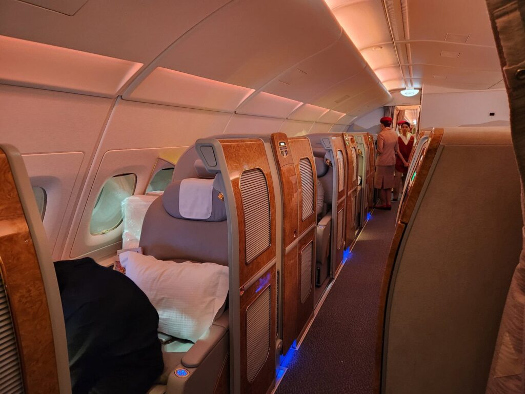 Cabine de première classe Emirates avec suites fermées et équipage en uniforme rouge à bord de l'appareil.