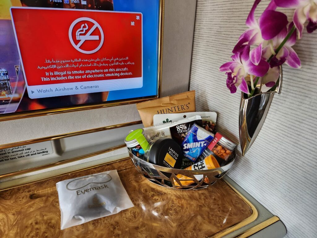 Suite Première Classe Emirates avec écran de bord, orchidées fraîches et panier de collations premium