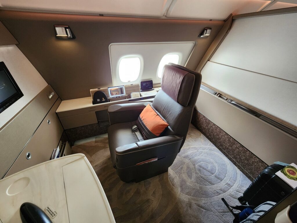 Suite de première classe Singapore Airlines avec large siège cuir, hublots et table de travail élégante.