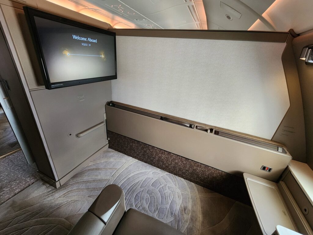 Suite fermée de Singapore Airlines en Première classe avec grand écran et sièges beiges luxueux.