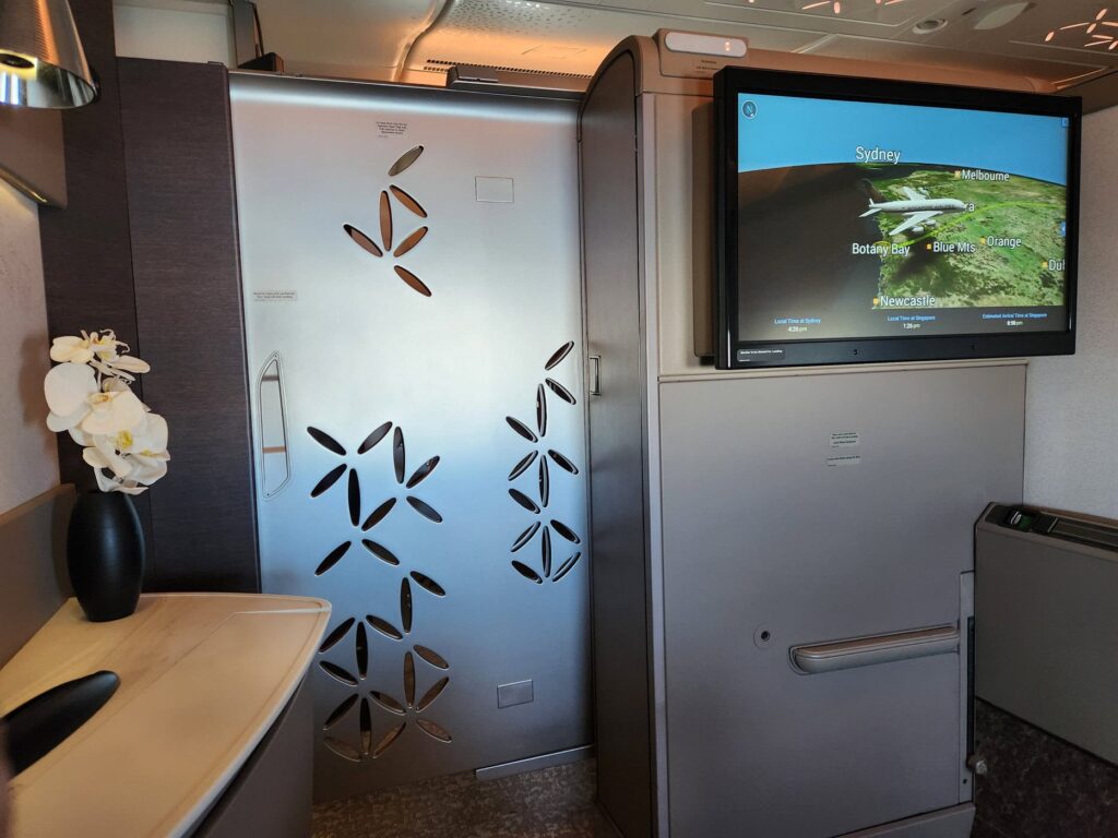 Suite fermée de première classe Singapore Airlines avec écran de vol affichant la route vers Sydney.