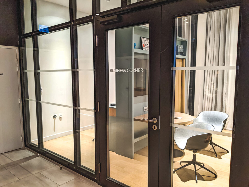 Espace business vitré avec bureau, chaises modernes grises et étagères dans le Courtyard by Marriott Paris Créteil.