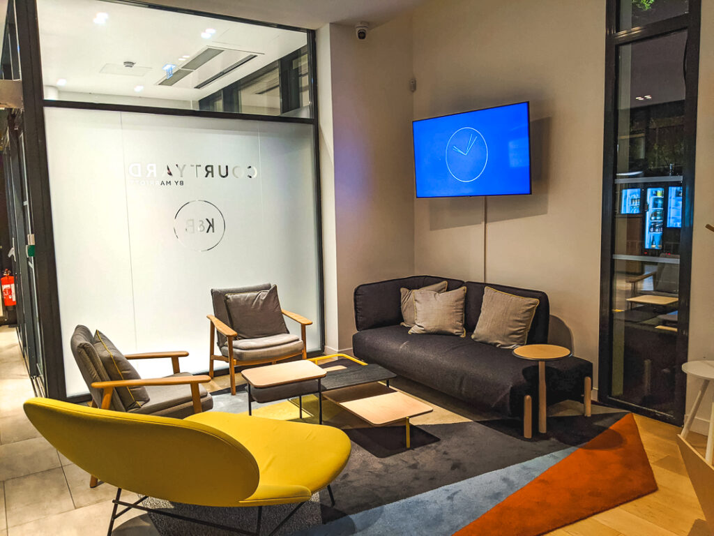 Salon moderne du Courtyard by Marriott Paris Créteil avec fauteuils design et écran mural allumé.