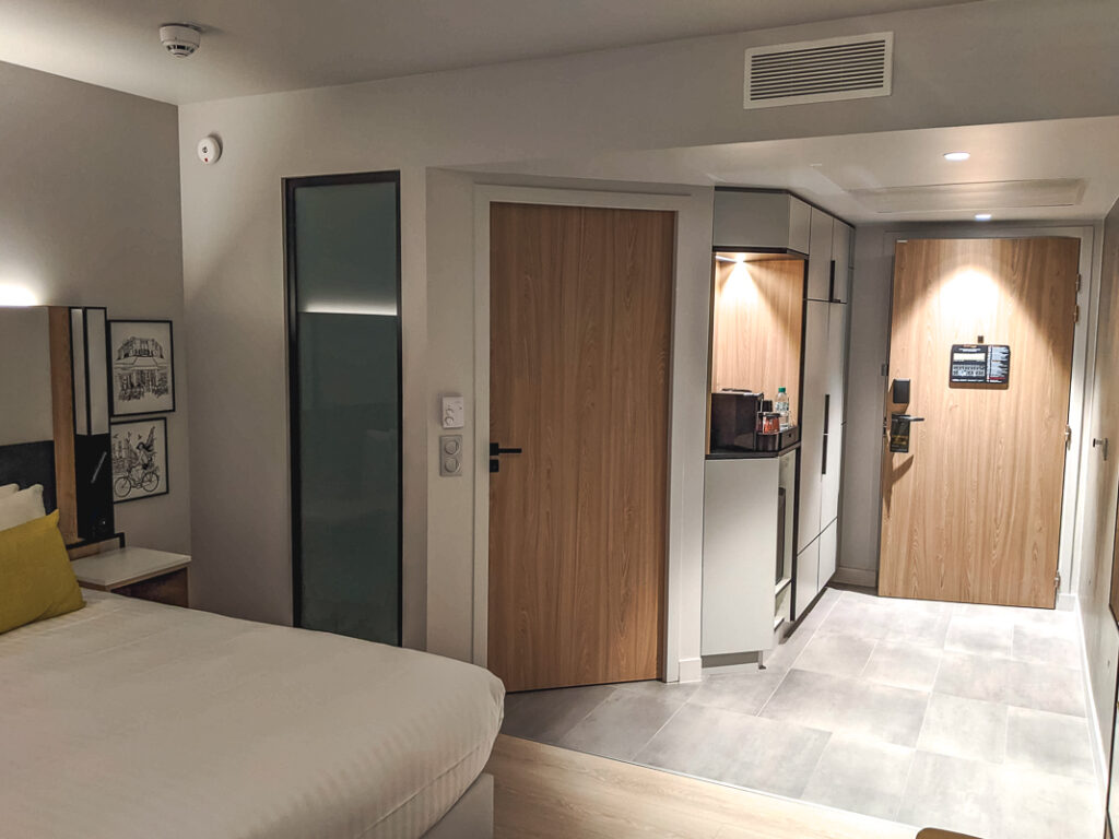 Chambre moderne du Courtyard Paris Créteil avec lit double, porte en bois et coin minibar éclairé.