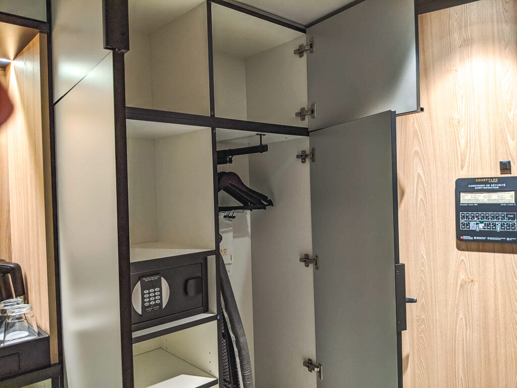 Penderie ouverte d'une chambre d'hôtel avec cintres, coffre-fort, planche à repasser et rangement supérieur.