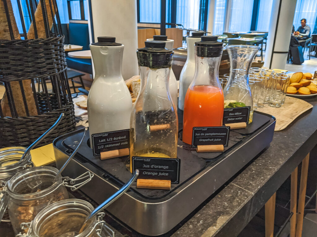 Carafes de jus, lait et eau détox disposées sur un buffet petit-déjeuner d'hôtel lumineux.