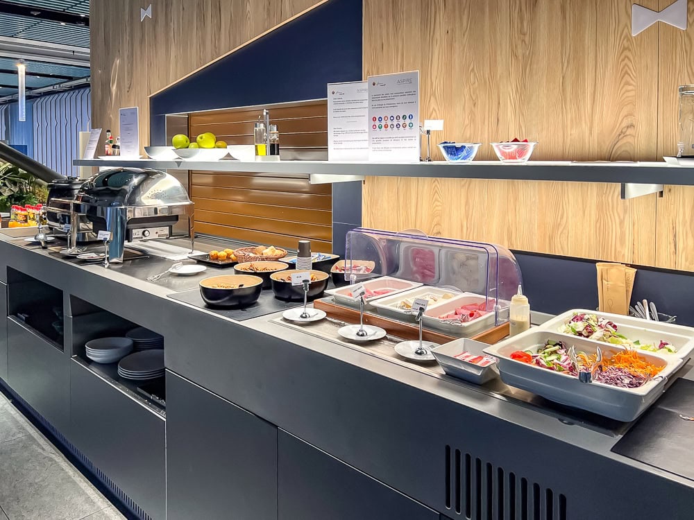Buffet froid et chaud du salon Aspire à l'aéroport de Genève avec plats variés et salades.
