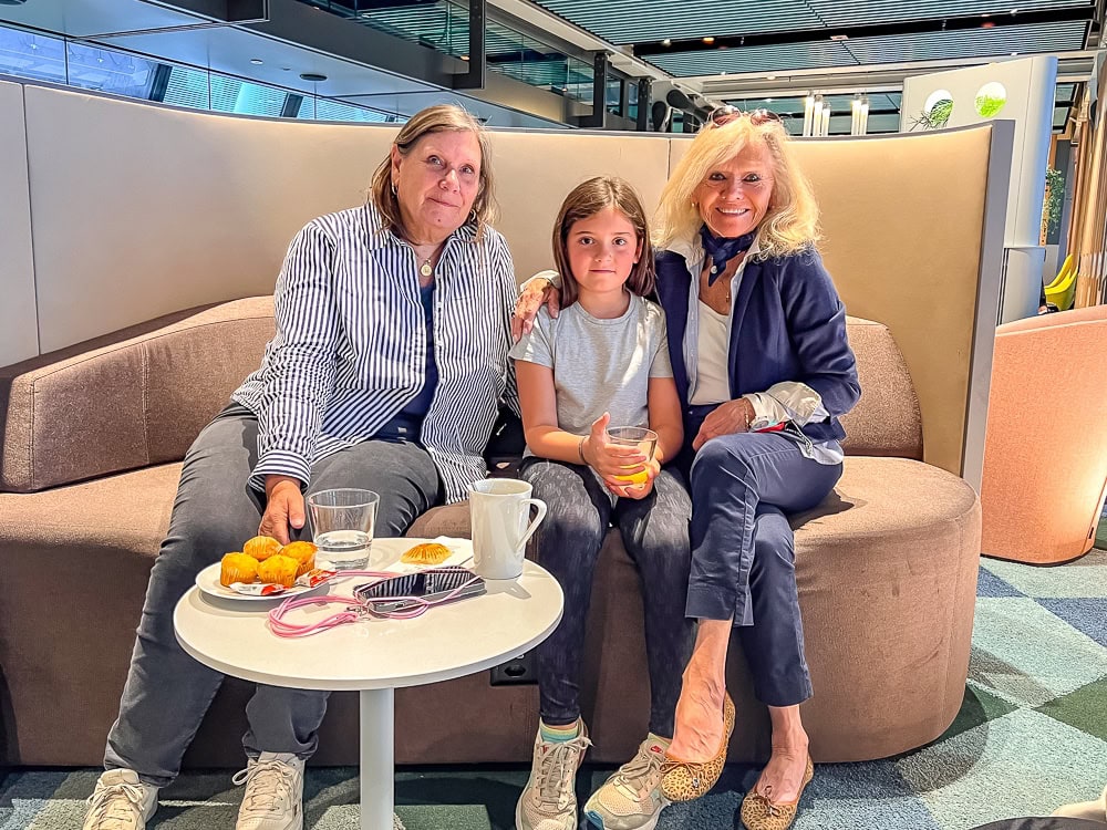 Trois voyageuses assises sur un canapé au salon Aspire de l'aéroport de Genève avec collations.