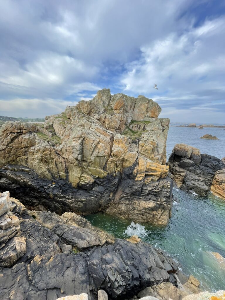 Falaises rocheuses du Gouffre de Plougrescant dominant une mer turquoise sous un ciel partiellement nuageux.