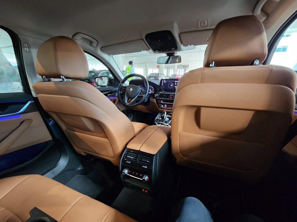 Intérieur en cuir brun d'un véhicule BMW avec tableau de bord lumineux et conducteur à l'avant.