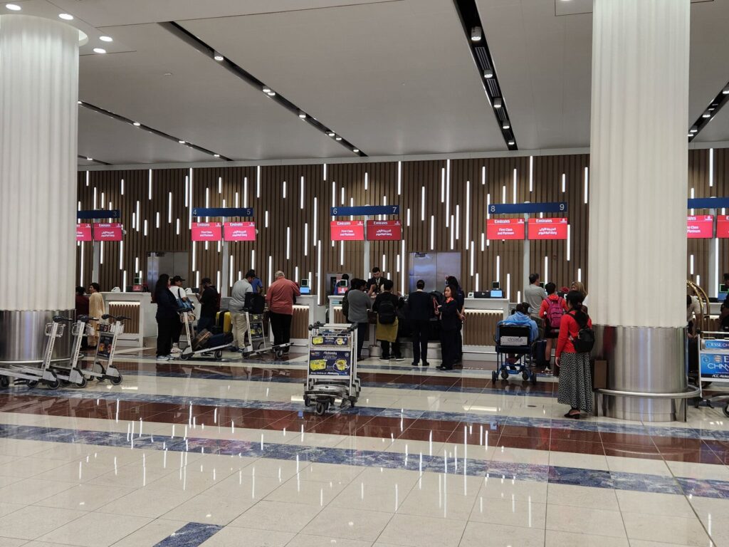 Comptoirs d'enregistrement Emirates pour la First Class avec passagers et chariots à l'aéroport de Dubaï.
