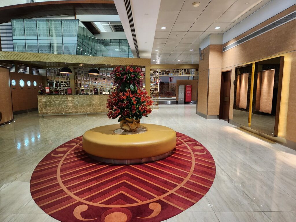 Hall d'accueil du lounge Emirates à l'aéroport de Dubaï avec comptoir doré et fleurs rouges.