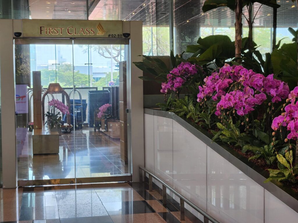 Entrée du salon First Class de Singapore Airlines avec des orchidées violettes et une lumière naturelle.