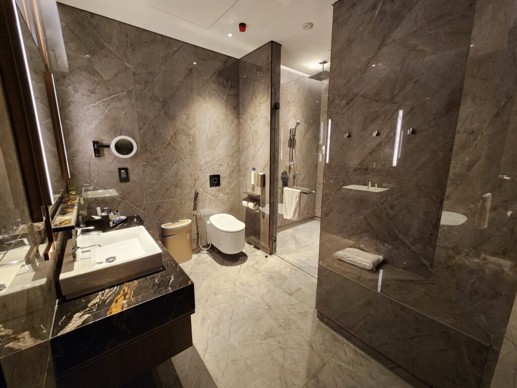 Salle de bain luxueuse en marbre avec douche vitrée, lavabo moderne et toilettes dans un lounge Singapore Airlines.