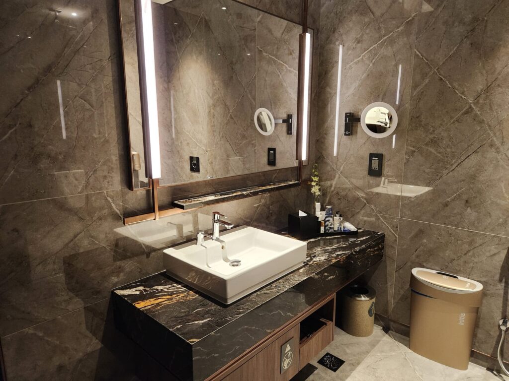 Salle de bain élégante au sol en marbre avec lavabo moderne et produits Singapore Airlines au comptoir.