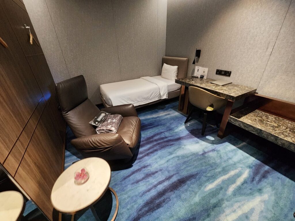 Chambre avec lit simple, fauteuil en cuir et bureau au lounge Singapore Airlines à l'aéroport de Changi.