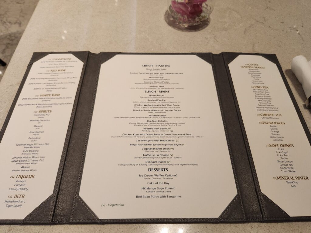 Menu du salon Singapore Airlines avec plats, boissons et desserts présentés sur comptoir en marbre clair.