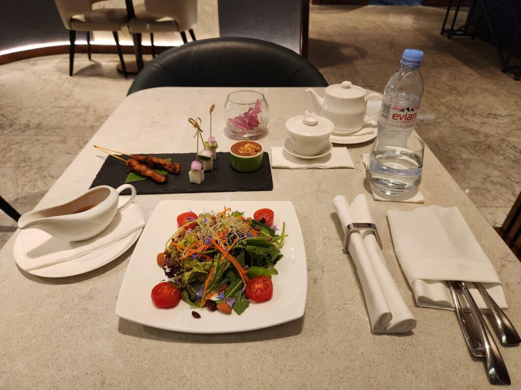 Repas raffiné servi dans le lounge de Singapore Airlines avec salade, brochettes et théière blanche.