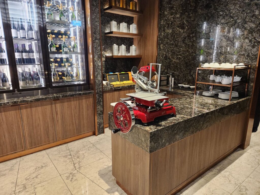 Zone de restauration du salon Singapore Airlines avec trancheuse rouge, vins et tasses blanches alignées.
