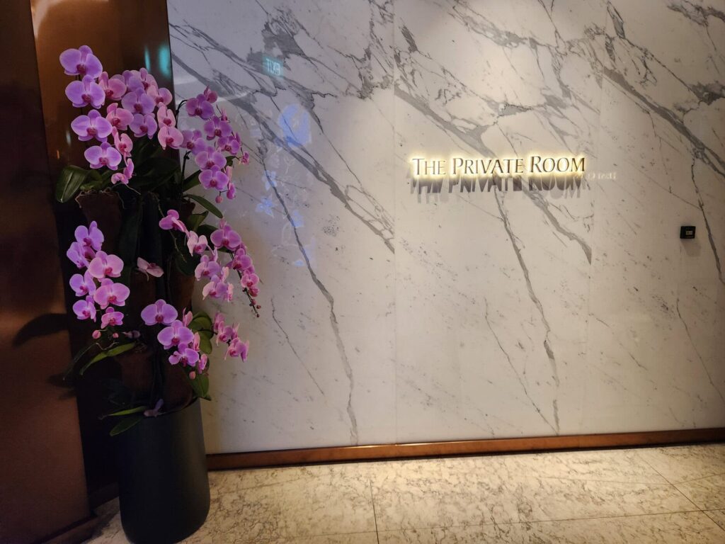 Entrée du salon The Private Room de Singapore Airlines avec mur en marbre et orchidées violettes.