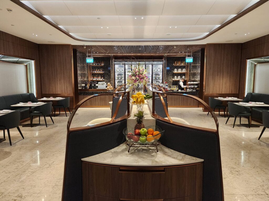 Salon Singapore Airlines avec fauteuils élégants, fruits frais et comptoir de restauration au style raffiné.