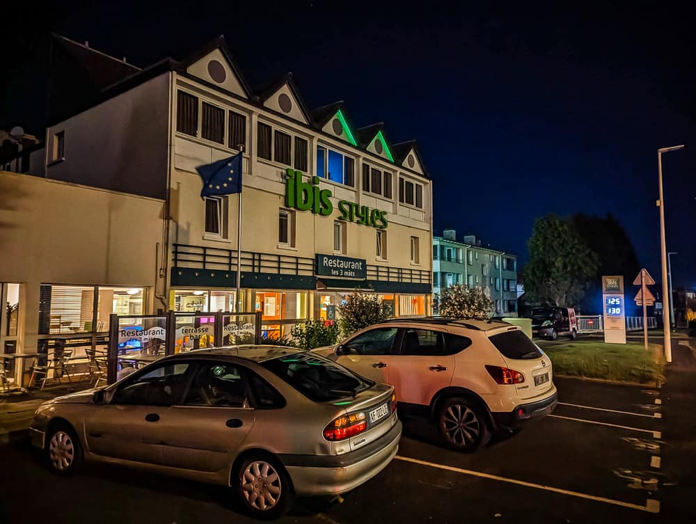 Façade nocturne de l'hôtel Ibis Styles Ouistreham avec enseigne verte éclairée et voitures stationnées devant